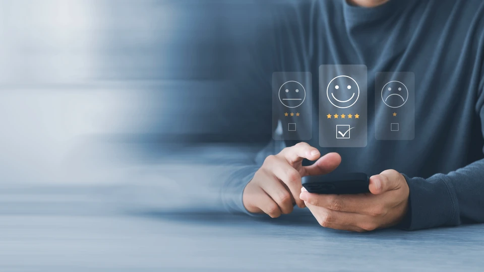 Technicien en combinaison bleue effectuant le remplacement d'un pare-brise automobile à l'extérieur, utilisant des ventouses de manutention professionnelles pour manipuler le vitrage. Véhicule blanc positionné sur aire de travail, outils spécialisés visibles.