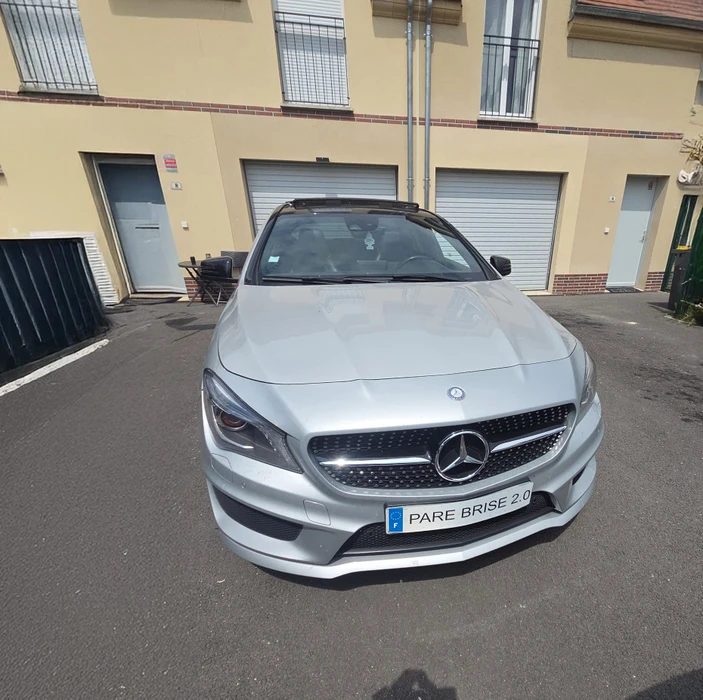 Scène extérieure d'un véhicule automobile avec pare-brise sale couvert de nombreuses fientes d'oiseaux et salissures. Rétroviseur latéral visible, environnement verdoyant en arrière-plan.