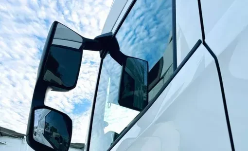 Atelier de maintenance et réparation de camions semi-remorques. Mécanicien travaillant sur cabine basculée rouge révélant châssis, moteur et transmission. Environnement industriel avec pont élévateur, outillage spécialisé.